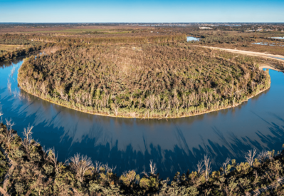 Aerial view of a river bending around a forested floodplain wetland, showing natural water flow and vegetation patterns in an Australian landscape.